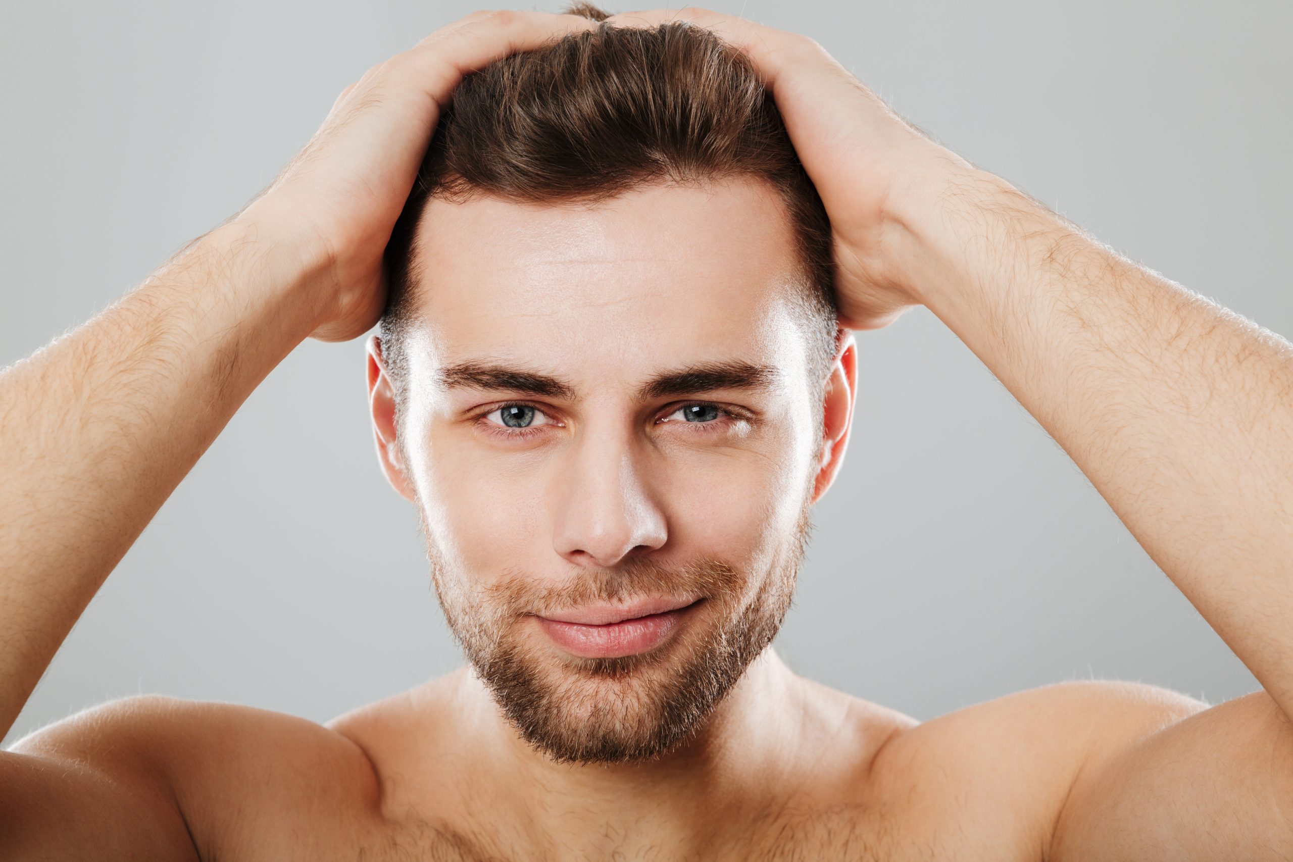 Close up portrait of a handsome man touching his hair isolated over gray background